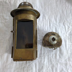 Peut inclure: Une lanterne ancienne en laiton avec un dessus en forme de dôme et une fenêtre rectangulaire en verre. La lanterne a une porte à charnière et un couvercle circulaire séparé. La lanterne est probablement utilisée à des fins décoratives.