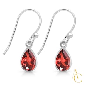 May include: A pair of silver drop earrings with pear-shaped, faceted red gemstones. The earrings have a simple design with a hook closure. The gemstones are set in a silver bezel.
