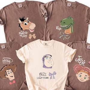 A collection of five t-shirts with cartoon character designs, including a cowboy, a dinosaur, and a girl.