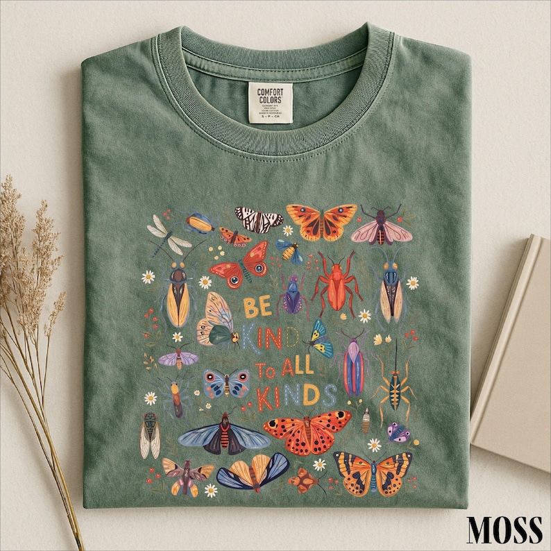 A green t-shirt with a colorful graphic design featuring various insects and butterflies, along with the text "Be kind to all kinds".