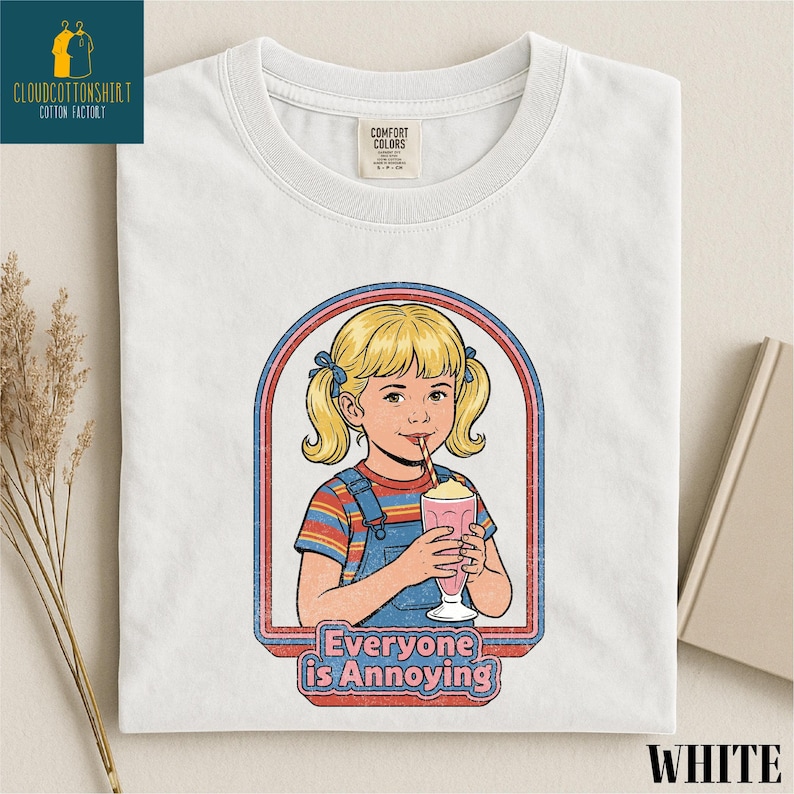 A white t-shirt with a graphic design depicting a young girl with blonde hair and a straw, holding a milkshake, with the text "Everyone is Annoying" below the image.