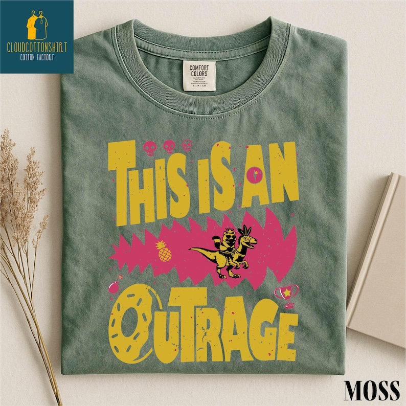 a green t-shirt with a colorful graphic design, including a dinosaur, flowers, and the text "This is an OTRAGE".