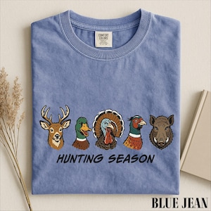 A blue t-shirt with a graphic design of various hunting animals, including a deer, turkey, duck, and boar, along with the text "HUNTING SEASON".