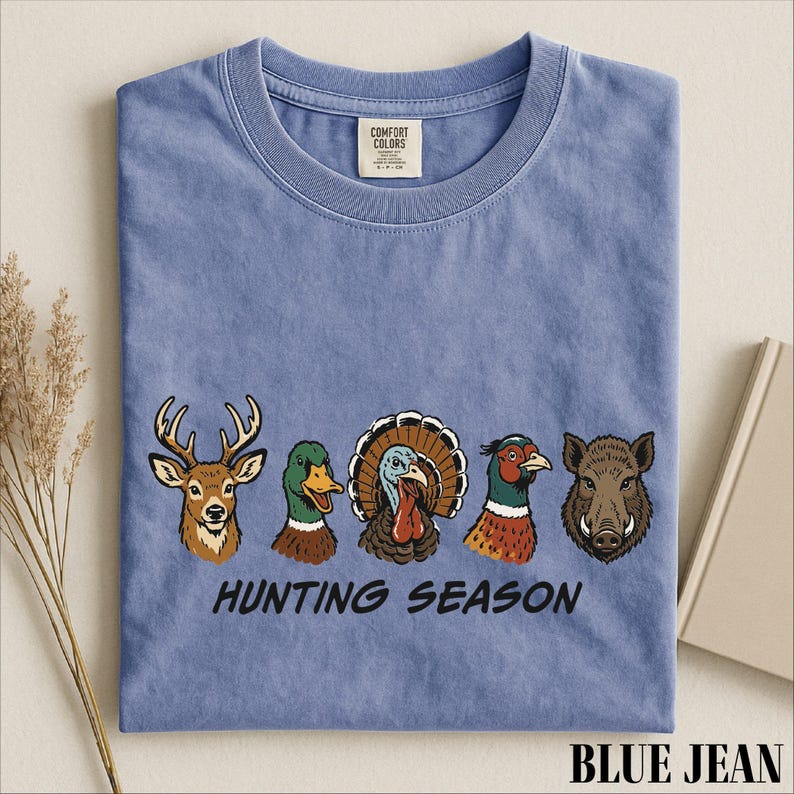 A blue t-shirt with a graphic design of various hunting animals, including a deer, turkey, duck, and boar, along with the text "HUNTING SEASON".