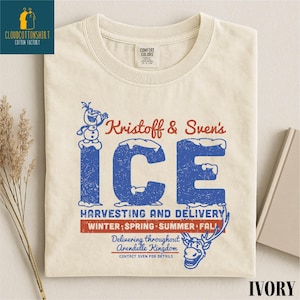 May include: Ivory-colored t-shirt featuring a distressed graphic with the text "Kristoff & Sven's ICE" in blue and red. The design includes a snowman, reindeer, and text about ice harvesting and delivery. The shirt is made of cotton.