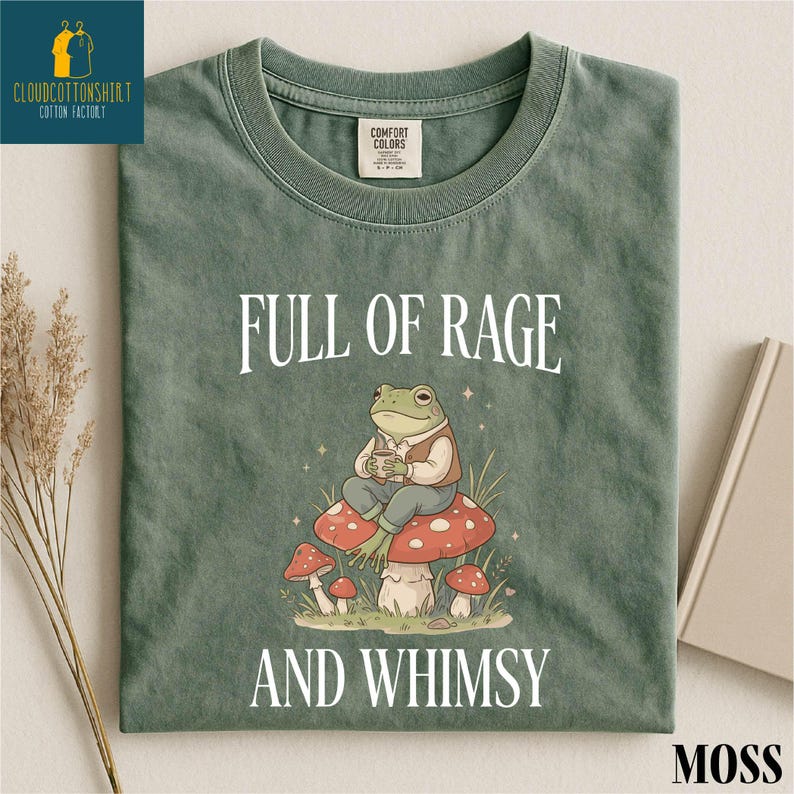 a green t-shirt with a cartoon frog sitting on a mushroom and surrounded by mushrooms, with the text "FULL OF RAGE AND WHIMSY" printed on it.