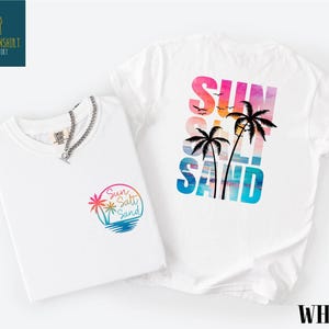a white t-shirt with a colorful graphic design on the back, depicting a beach scene with palm trees and a sunset.