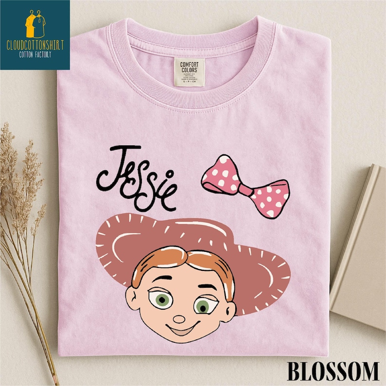 A pink t-shirt with a cartoon character and a pink polka dot bow, along with the text " Jessie" and "Blossom".