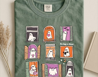 Może przedstawiać: Mchowo-zielony t-shirt z okrągłym dekoltem i nadrukiem graficznym przedstawiającym różne duchy w oknach. Wzór zawiera duchy czytające, słuchające muzyki, rozmawiające przez telefon i wieszające pranie, z białym napisem Too Cozy to Haunt.