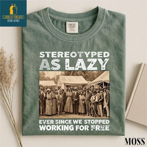 May include: Moss green t-shirt with the text "STEREOTYPED AS LAZY EVER SINCE WE STOPPED WORKING FOR FREE" in white. The shirt features a sepia-toned image of a group of people. The shirt has a Comfort Colors tag.