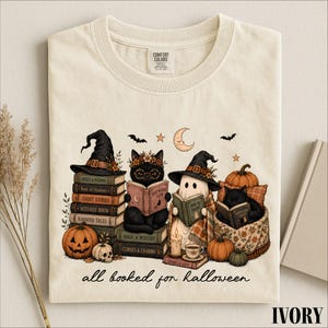 A t-shirt with a Halloween-themed illustration depicting a witch, cat, ghost, pumpkin, and books, along with the text "all read for Halloween".