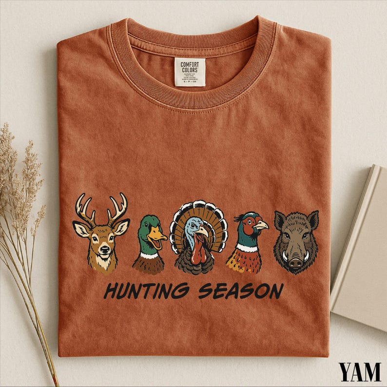 a brown t-shirt with a graphic design of various bird species, including a turkey, a duck, a goose, and a boar, along with the text "HUNTING SEASON".