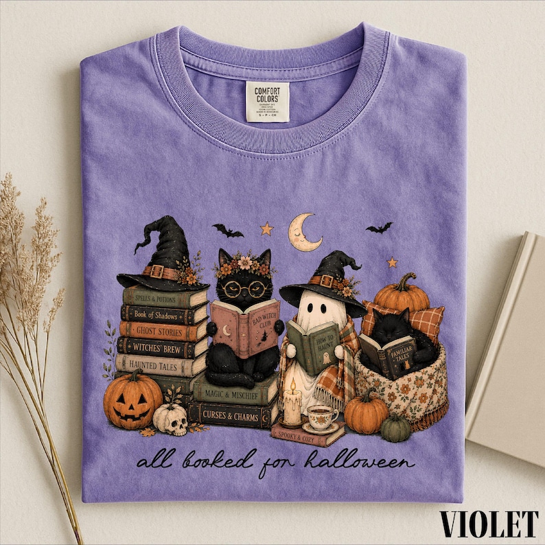 A purple t-shirt with a Halloween-themed illustration of a witch, cat, ghost, pumpkin, and books, along with the text "all read for Halloween".