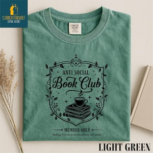 May include: Light green t-shirt with a black graphic that reads "Anti Social Book Club" with a coffee cup on top of books. The shirt also has the text "Member Only" and "Making friends with characters, not people."