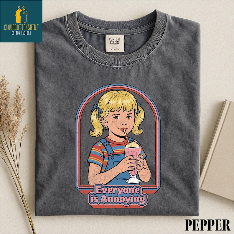 a gray t-shirt with a graphic design depicting a young girl with blonde hair and a straw, holding a pink drink. The text below the graphic reads "Everyone is Annoying".