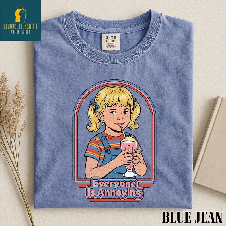 a blue t-shirt with a graphic design depicting a young girl with blonde hair and a straw, holding a pink drink. The text below the graphic reads "Everyone is Annoying".