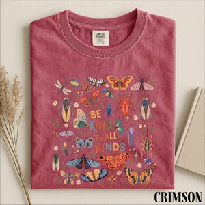 A red t-shirt with a colorful graphic design of various insects and butterflies, along with the text "Be kind to all kinds".