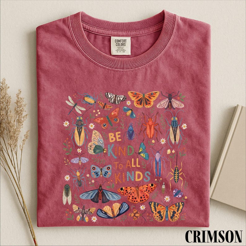 A red t-shirt with a colorful graphic design of various insects and butterflies, along with the text "Be kind to all kinds".