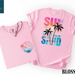 two pink t-shirts with a beach-themed design, including palm trees and a sunset.