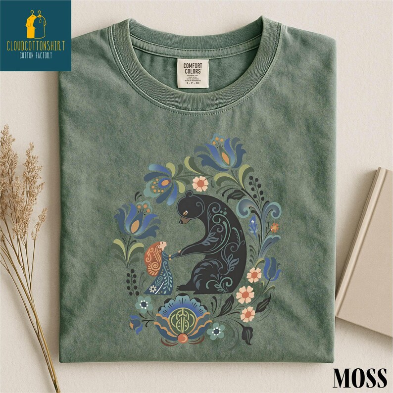 a green t-shirt with a colorful floral and animal design, including a black bear, flowers, and other elements.