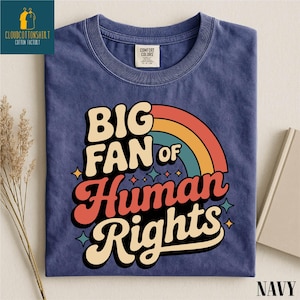May include: Navy blue t-shirt with the text "BIG FAN of Human Rights" in a retro font and a rainbow graphic. The shirt has a crew neck and is made of a soft, comfortable material. The shirt is folded and displayed on a neutral background.
