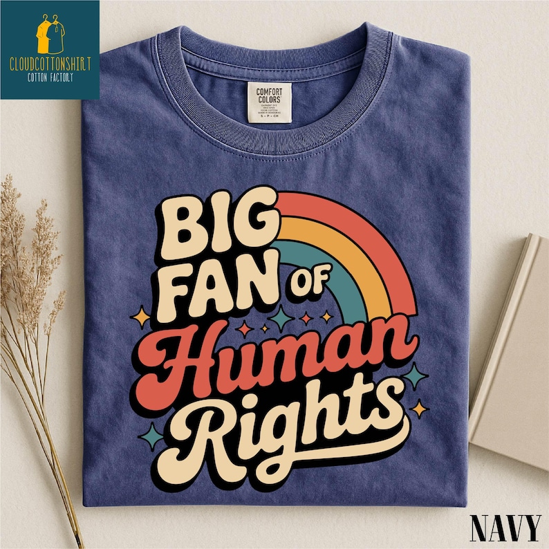 May include: Navy blue t-shirt with the text "BIG FAN of Human Rights" in a retro font and a rainbow graphic. The shirt has a crew neck and is made of a soft, comfortable material. The shirt is folded and displayed on a neutral background.