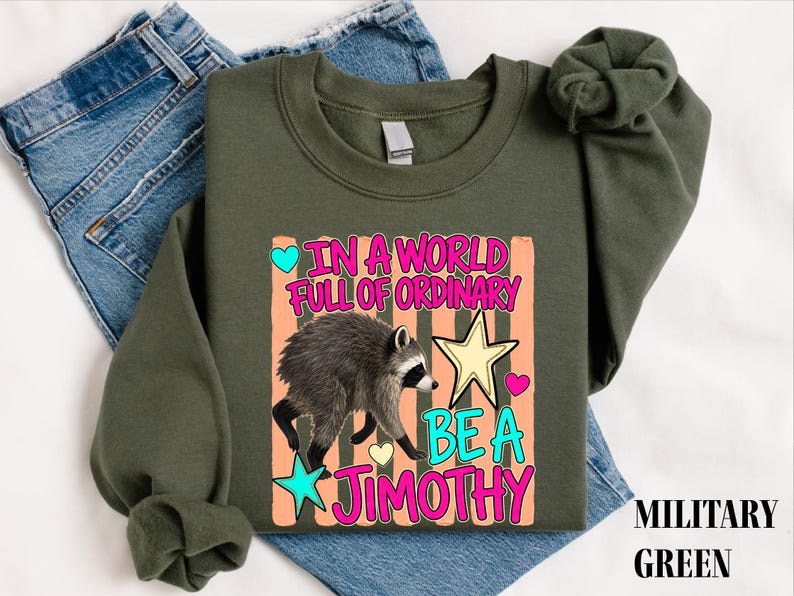 A military green sweatshirt with a graphic design featuring a raccoon and the text "In a world full of ordinary, be a jimothy"