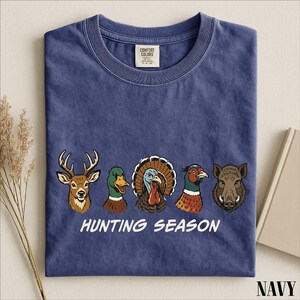 A navy blue t-shirt with a graphic design of various hunting animals, including a deer, turkey, duck, and boar, along with the text "HUNTING SEASON".