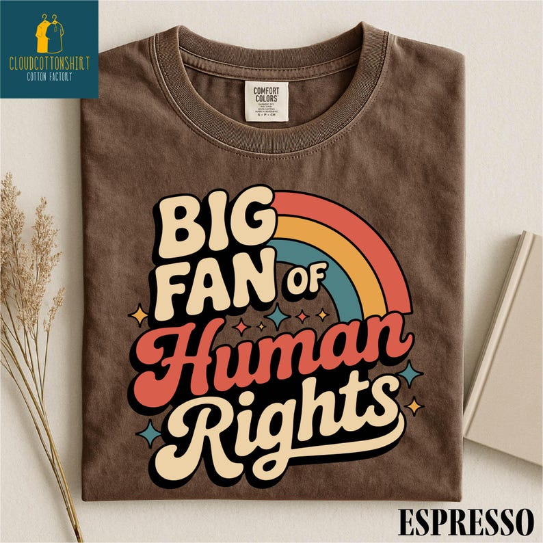 May include: Espresso-colored t-shirt with the text "BIG FAN of Human Rights" in a retro font, featuring a rainbow design. The shirt has a crew neck and a Comfort Colors tag.