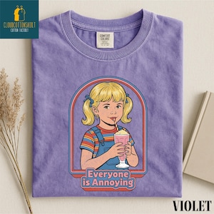 a purple t-shirt with a graphic design depicting a young girl with blonde hair and a straw, holding a pink drink. The text below the graphic reads "Everyone is Annoying".