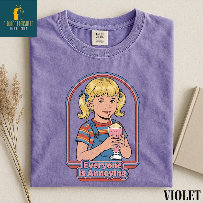 a purple t-shirt with a graphic design depicting a young girl with blonde hair and a straw, holding a pink drink. The text below the graphic reads "Everyone is Annoying".