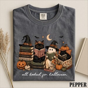A t-shirt with a Halloween-themed graphic design featuring a witch, a cat, a ghost, and a pumpkin, along with the text "all read for Halloween".
