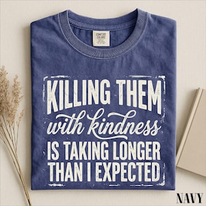 A navy blue t-shirt with a white text design that reads "Killing them with kindness is taking longer than I expected".