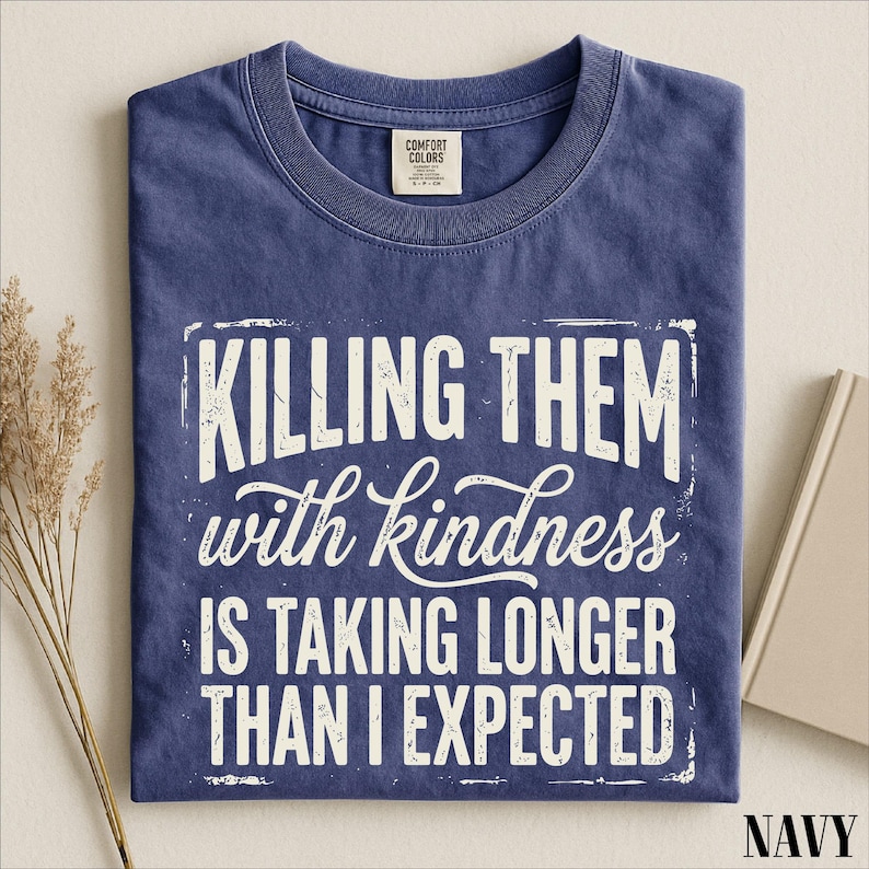 A navy blue t-shirt with a white text design that reads "Killing them with kindness is taking longer than I expected".