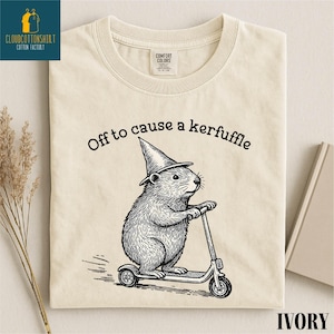 A t-shirt with a cartoon image of a hamster riding a scooter, wearing a pointy hat, and the text "Off to cause a kerfluffle" printed on it.