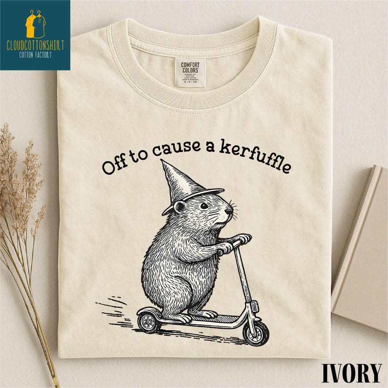A t-shirt with a cartoon image of a hamster riding a scooter, wearing a pointy hat, and the text "Off to cause a kerfluffle" printed on it.