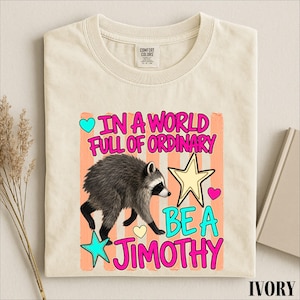 A white t-shirt with a colorful graphic design featuring a raccoon and text that reads "In a world full of ordinary, be a jimothy".