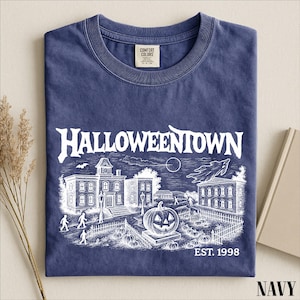 A navy blue t-shirt with a Halloween-themed graphic design, including a castle, pumpkins, and a moon, along with the text "Halloweentown EST. 1998".