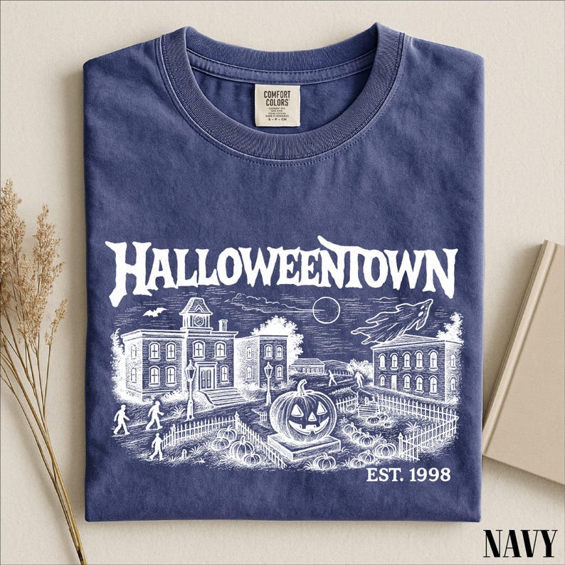 A navy blue t-shirt with a Halloween-themed graphic design, including a castle, pumpkins, and a moon, along with the text "Halloweentown EST. 1998".