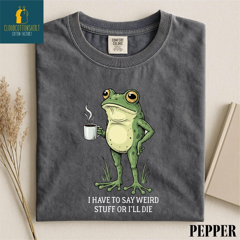 A gray t-shirt with a cartoon frog holding a cup of coffee and the text "I HAVE TO SAY WEIRD STUFF OR I'll die" printed on it.