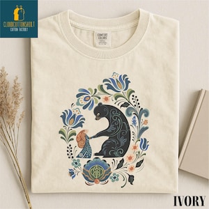 a white t-shirt with a colorful, intricate design depicting a bear surrounded by flowers and leaves.