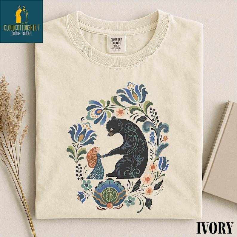 a white t-shirt with a colorful, intricate design depicting a bear surrounded by flowers and leaves.