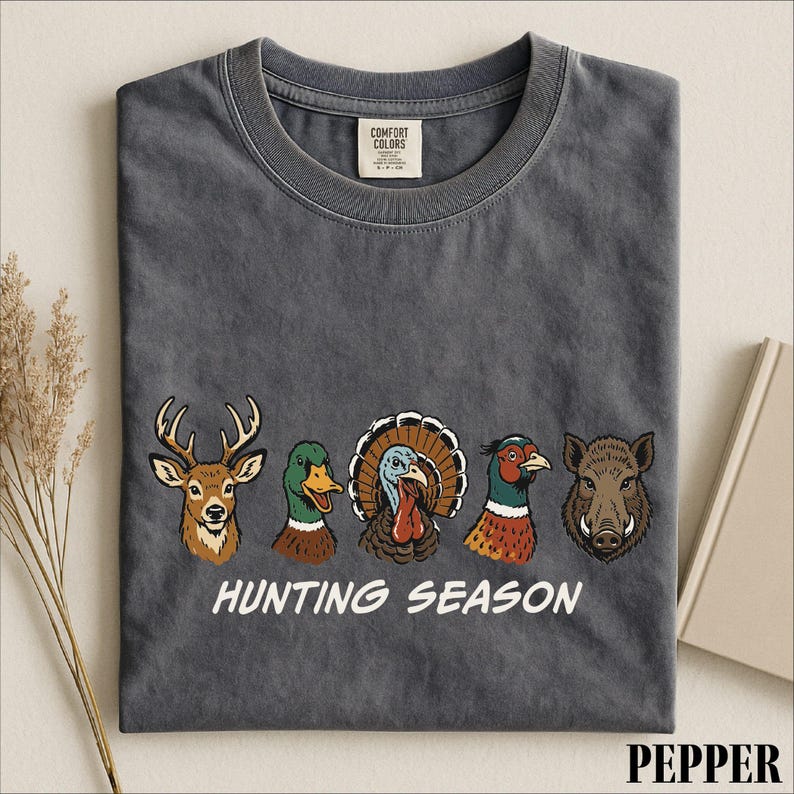 A gray t-shirt with a graphic design featuring four different animal heads, including a deer, a turkey, a boar, and a duck, along with the text "HUNTING SEASON".