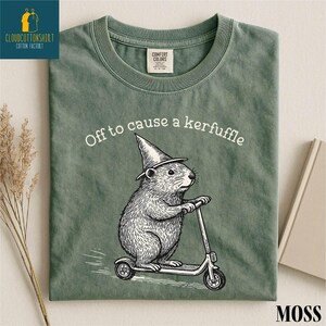 A green t-shirt with a cartoon image of a hamster riding a scooter, along with the text "Off to cause a kerfluffle" printed on it.