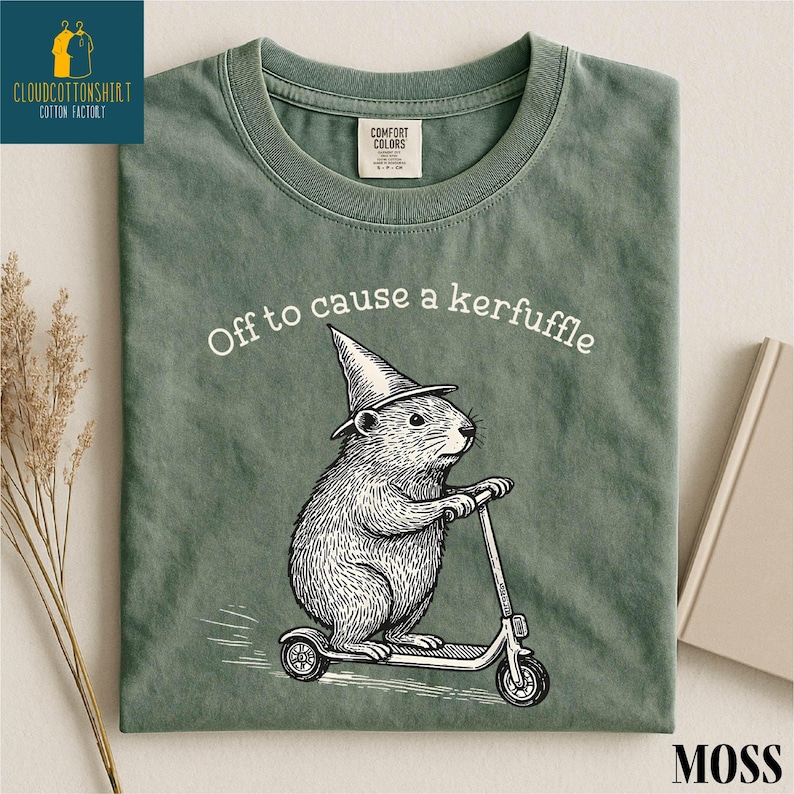 A green t-shirt with a cartoon image of a hamster riding a scooter, along with the text "Off to cause a kerfluffle" printed on it.