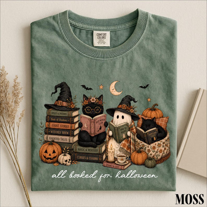 A green t-shirt with a Halloween-themed illustration of a witch, cat, ghost, pumpkin, and books, along with the text "all read for Halloween" and a label that says "COMFORT CLUB".