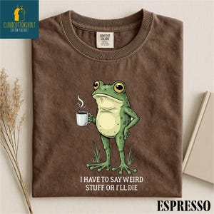 a brown t-shirt with a cartoon frog holding a cup of coffee and the text "I HAVE TO SAY WEIRD STUFF OR ILL DIE" printed on it.