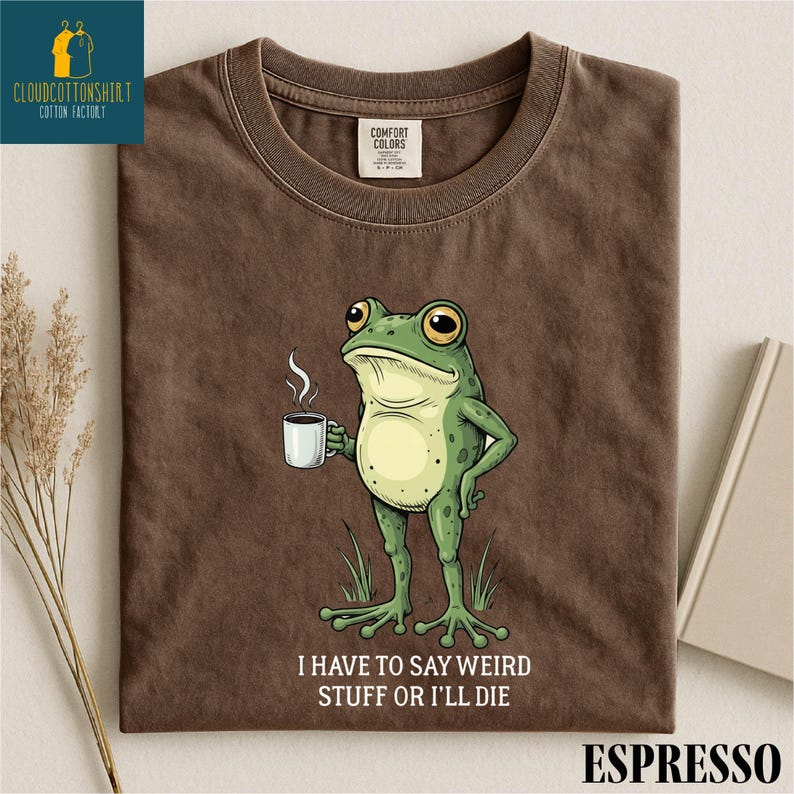 a brown t-shirt with a cartoon frog holding a cup of coffee and the text "I HAVE TO SAY WEIRD STUFF OR ILL DIE" printed on it.