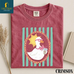 A red t-shirt with a cartoon image of a duck wearing sunglasses and holding a drink, surrounded by a decorative border.