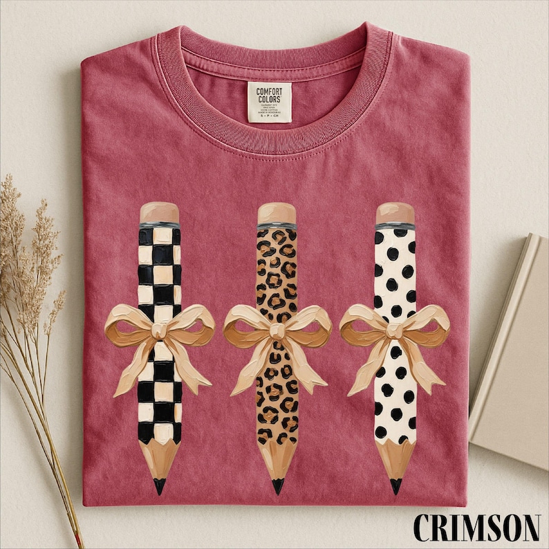 a pink t-shirt with three pencils, each with a unique design, and bows tied around them.